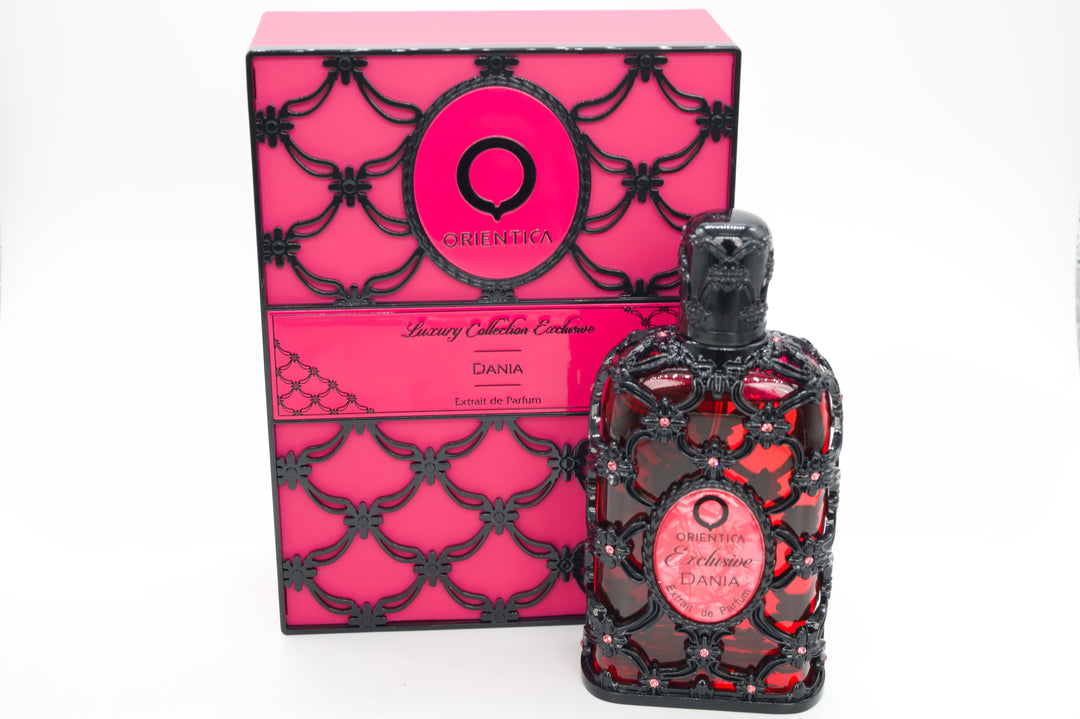 A bottle of Qshemika Dania Luxury Collection Extrait de Parfum next to its pink and black patterned packaging box, set against a plain white background.